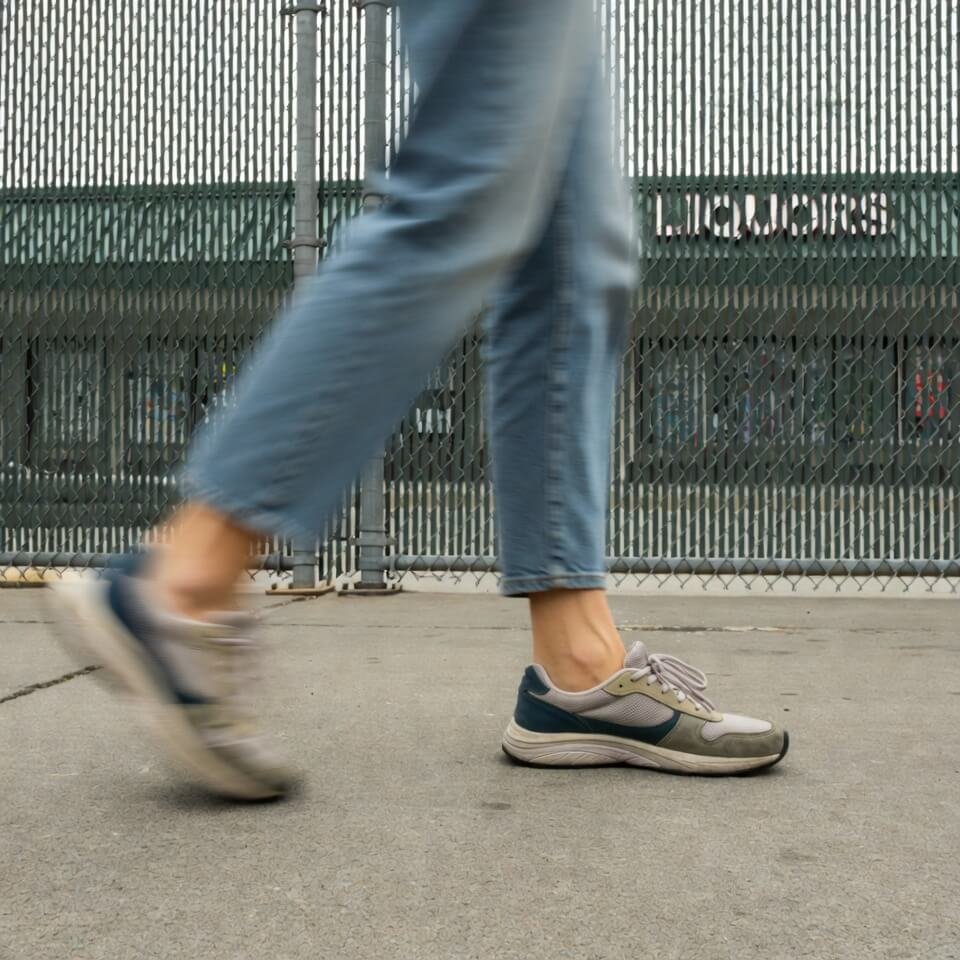 Blurry side shot of legs in sneakers walking past chain-link fence